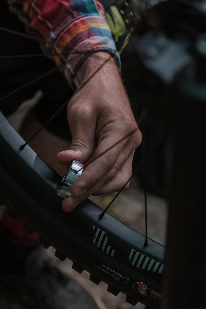 Detailed view of a hand using a tool to adjust bicycle spokes in an outdoor setting.